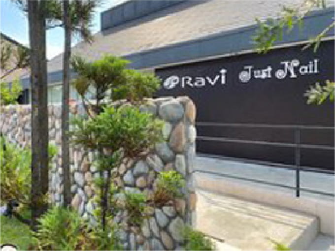 自然石を積み上げた壁と緑豊かな植物が並ぶ「RAVI Just Nail」と書かれたサロンの外観