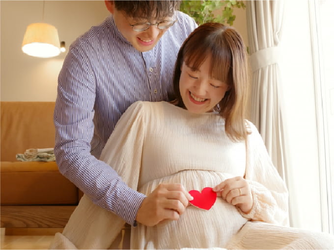 妊娠中の女性がお腹に赤いハートの飾りを当て、笑顔で楽しんでいる様子
