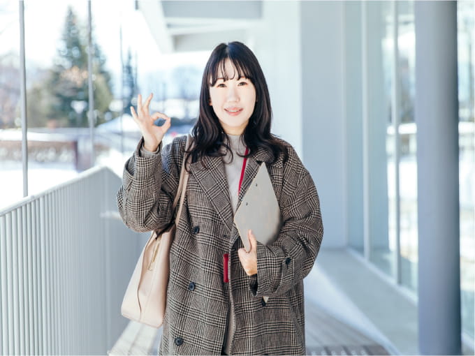 冬の屋外でチェック柄のコートを着た女性が、笑顔で「OK」のポーズをしている