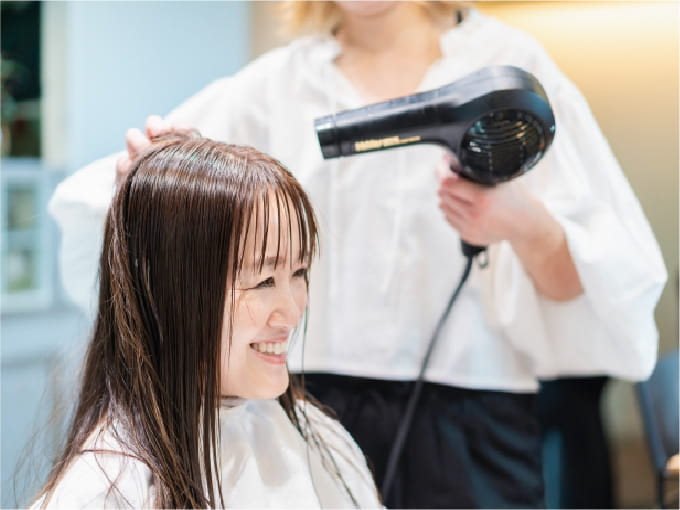 美容室で髪をドライヤーで乾かしてもらっている女性