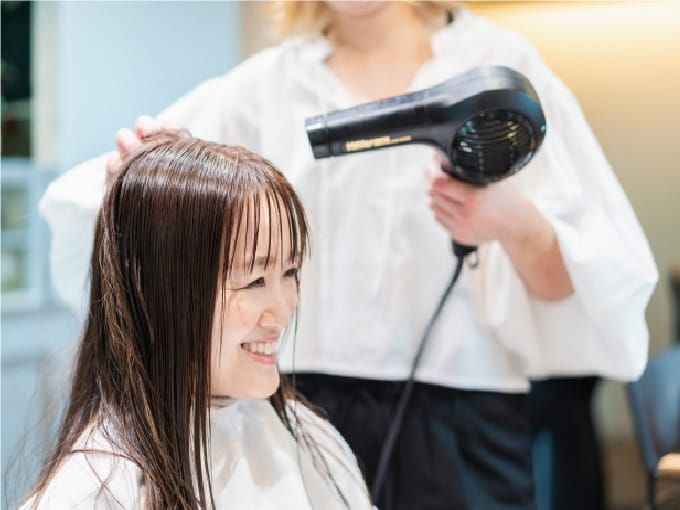 美容室で髪をドライヤーで乾かしてもらっている女性